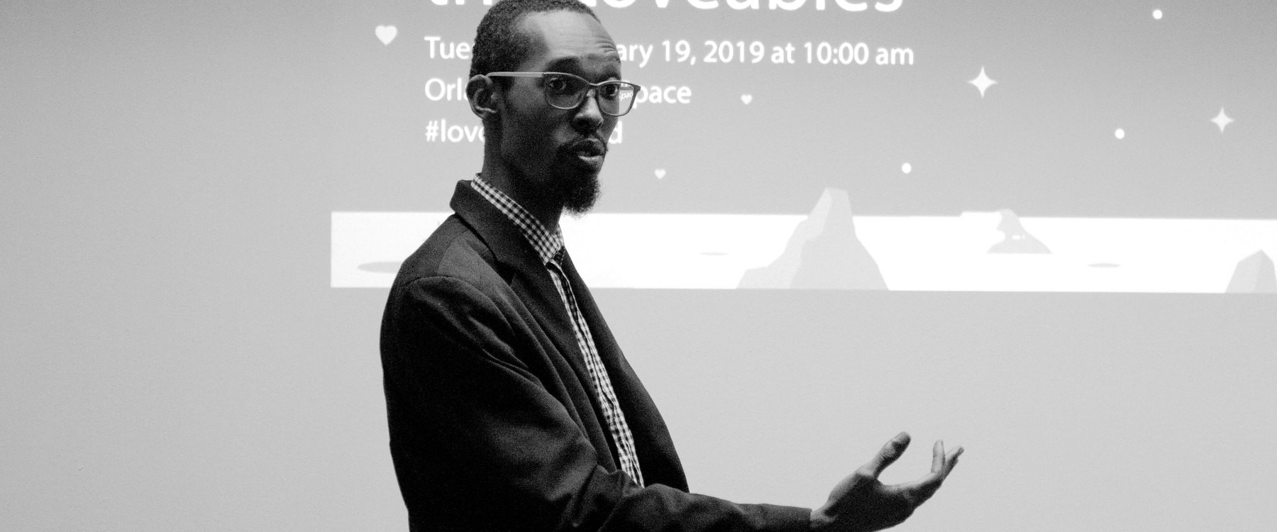 David mid-sentence in front of a projected title slide, one hand open toward the room