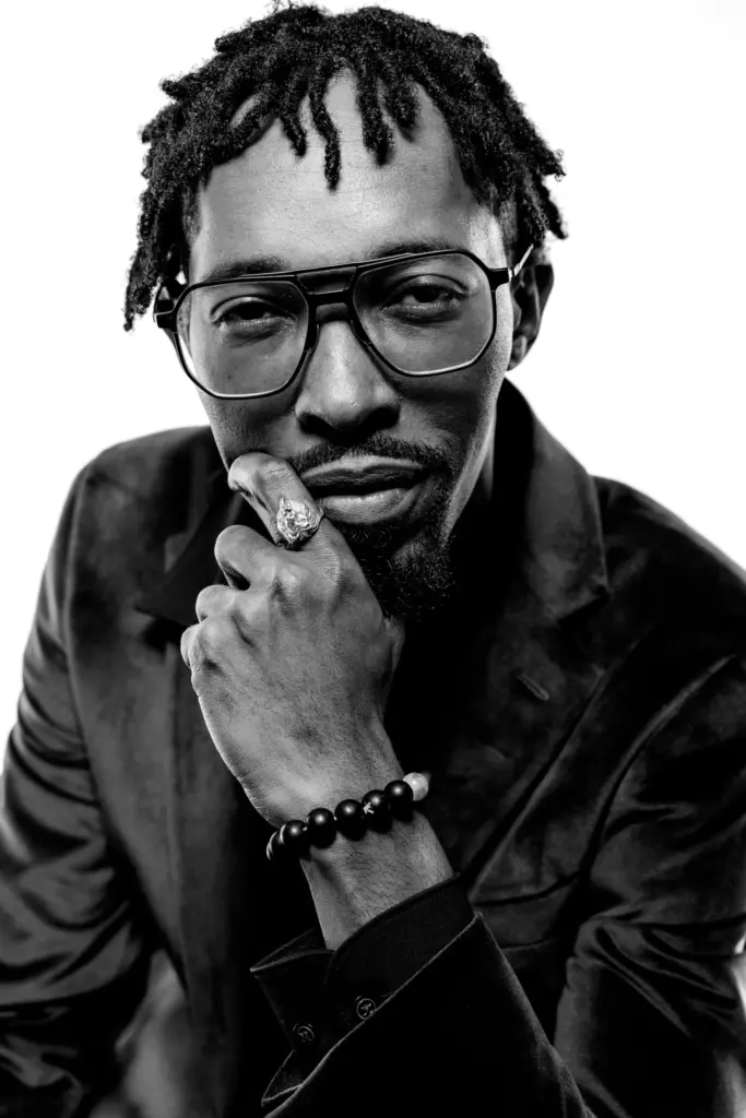David Yarde in black and white, a hand at his chin, wearing glasses